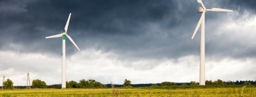 Windturbinen in ländlicher Landschaft unter stürmischem Himmel – Notwendigkeit des Ausbaus erneuerbarer Energiequellen laut Prognos AG