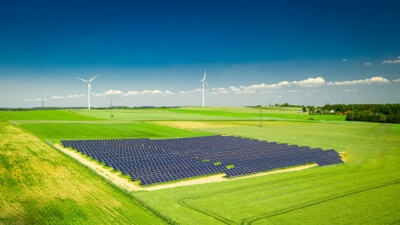 Weitläufige Photovoltaikanlage auf einem Feld mit Windkraftanlagen im Hintergrund, symbolisiert den Ausbau erneuerbarer Energien gemäß EEG 2025