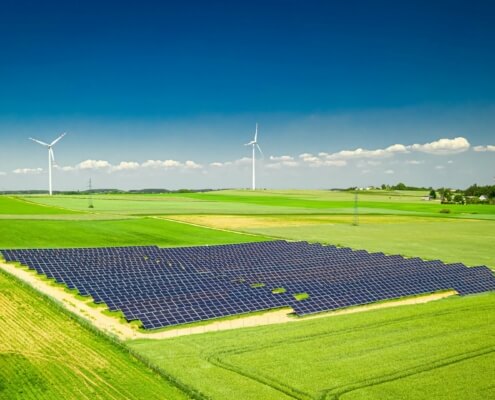 Weitläufige Photovoltaikanlage auf einem Feld mit Windkraftanlagen im Hintergrund, symbolisiert den Ausbau erneuerbarer Energien gemäß EEG 2025