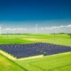 Weitläufige Photovoltaikanlage auf einem Feld mit Windkraftanlagen im Hintergrund, symbolisiert den Ausbau erneuerbarer Energien gemäß EEG 2025