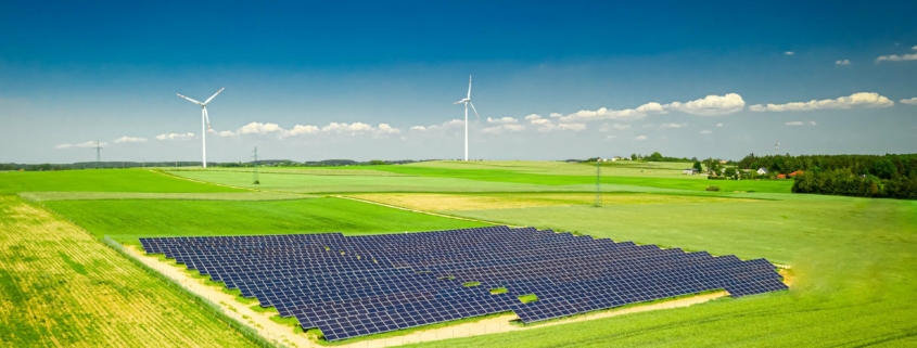 Weitläufige Photovoltaikanlage auf einem Feld mit Windkraftanlagen im Hintergrund, symbolisiert den Ausbau erneuerbarer Energien gemäß EEG 2025